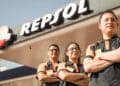 Dos hombres y una mujer con uniforme de empleado de estación de servicio, posan con los brazos cruzados delante de una estación de servicio donde se ve el logo de repsol